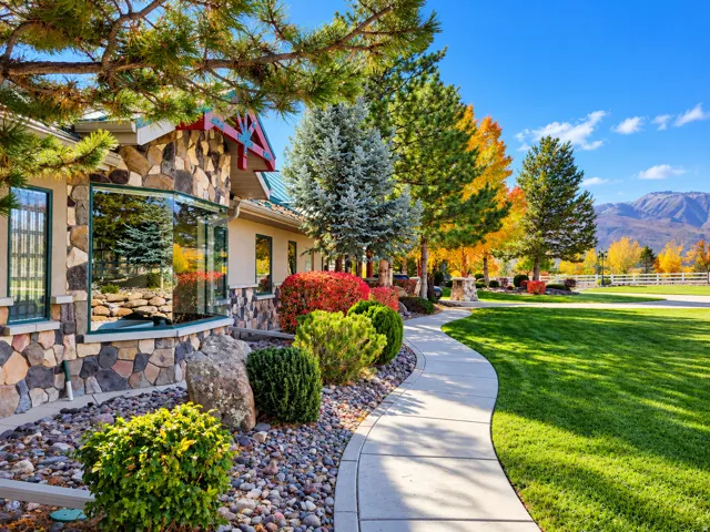 Stone facade with a bay window, manicured lawn, paved walkway, and mature landscaping