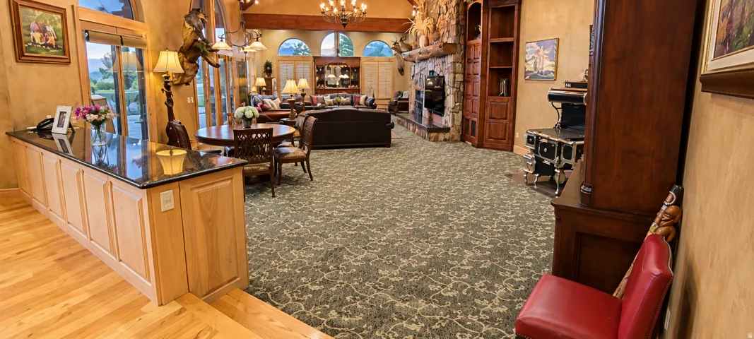 Hardwood flooring, kitchen island with dark countertop, multiple arched windows, stone-clad fireplace, and an ornate chandelier