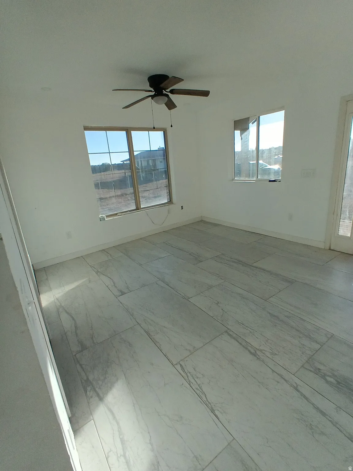 Unfurnished room featuring healthy amount of natural light, a ceiling fan, and light marble finish flooring