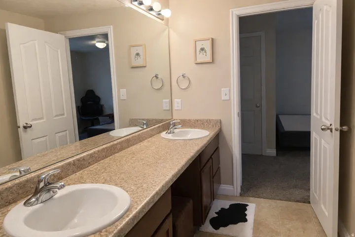 Full bathroom featuring double vanity, light carpet, and light tile patterned flooring