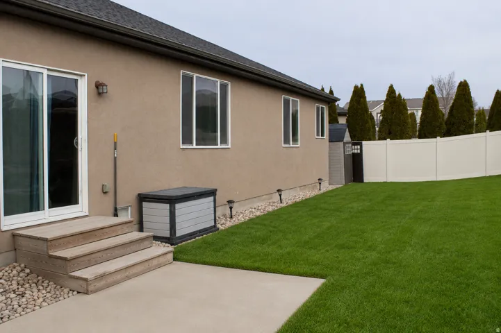 Expansive green lawn with a concrete patio, a three-step wooden deck, and a white privacy fence.  AI Adjusted Photo