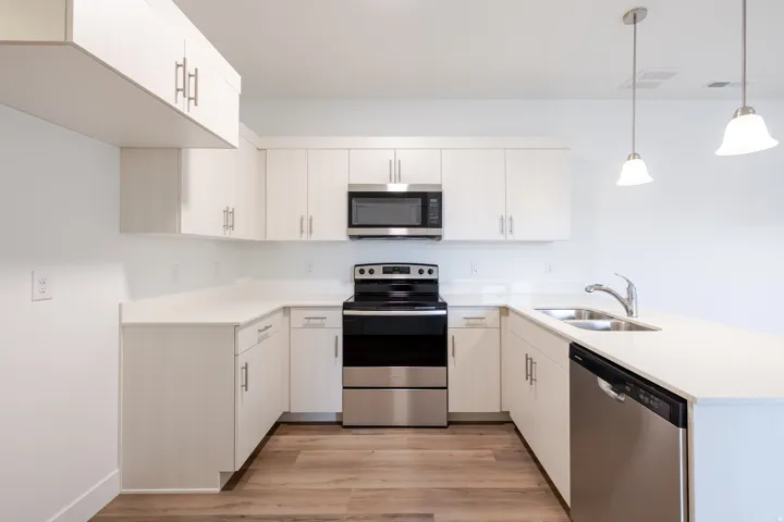 Contemporary kitchen featuring white cabinetry, light-toned countertops, stainless steel appliances, and wood-finish flooring