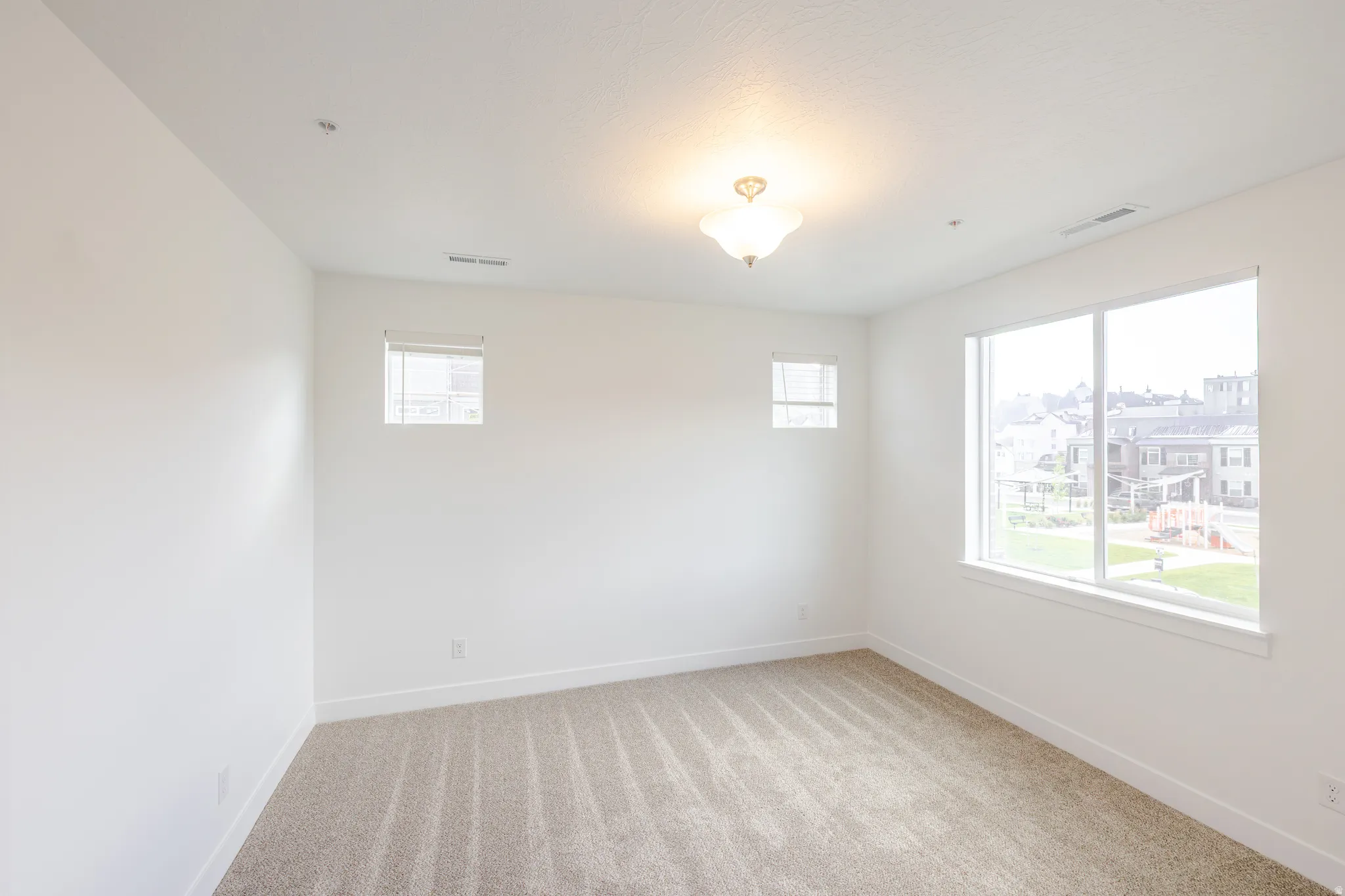 Bright room featuring neutral-toned carpet, white walls, and a large picture window with two smaller windows offering multiple exposures