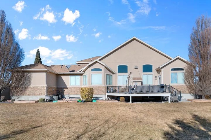 Rear view of house featuring a wooden deck, stucco siding, a lawn, and brick siding