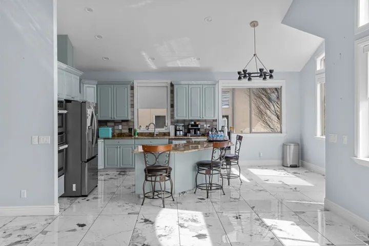 Kitchen with dark stone countertops, a kitchen island, stainless steel fridge with ice dispenser, a kitchen breakfast bar, and vaulted ceiling