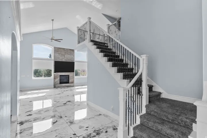 Staircase featuring a high ceiling, a premium fireplace, marble finish flooring, and a ceiling fan