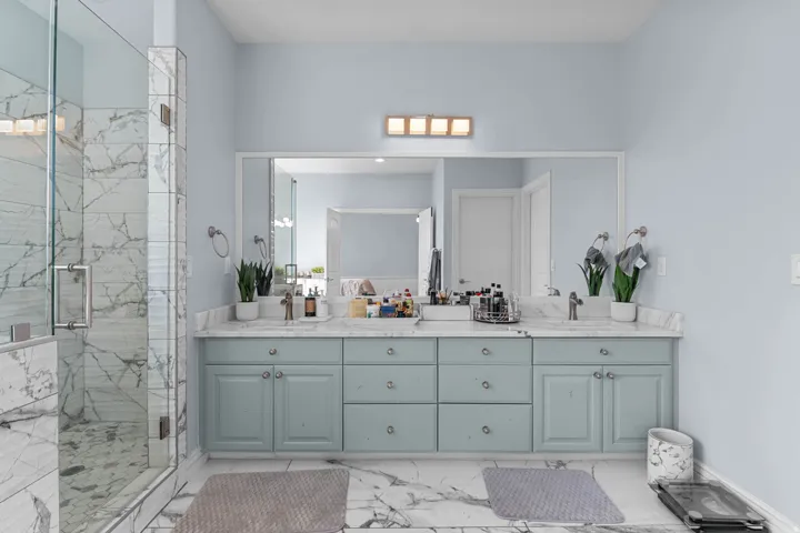 Bathroom with double vanity, a marble finish shower, and light marble finish flooring