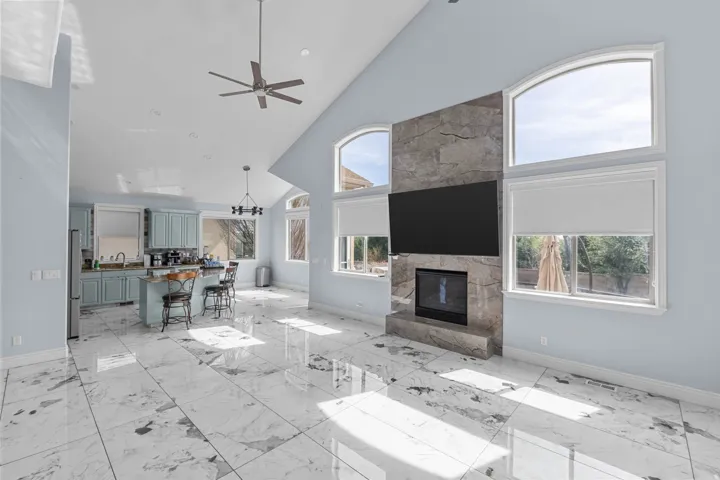 Living room featuring lofted ceiling, a chandelier, ceiling fan, light marble finish flooring, and a fireplace