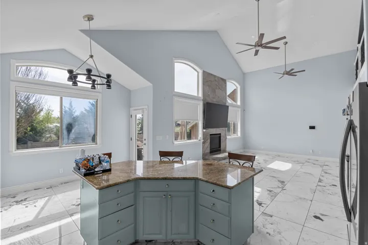 Kitchen with open floor plan, a high ceiling, a large fireplace, a ceiling fan, and dark stone counters