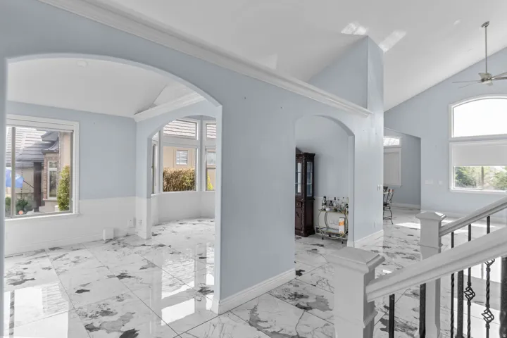 Corridor with lofted ceiling, arched walkways, healthy amount of natural light, and light marble finish flooring