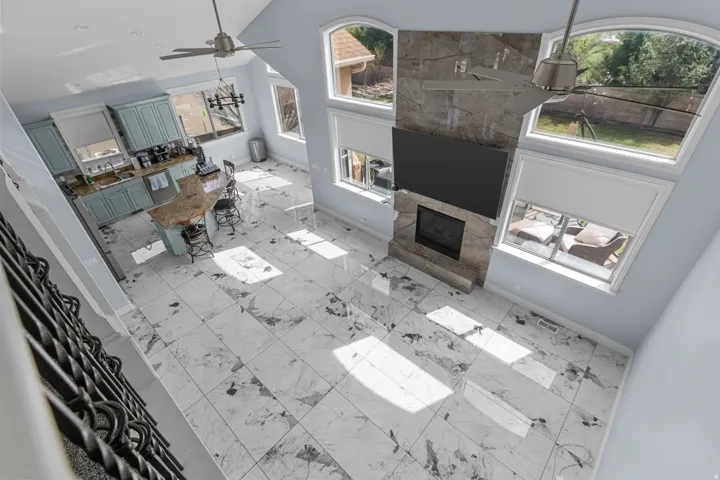 Living area featuring ceiling fan, vaulted ceiling, a fireplace, and light marble finish flooring
