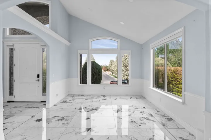 Foyer entrance with arched walkways, light marble finish floors, vaulted ceiling, plenty of natural light, and wainscoting