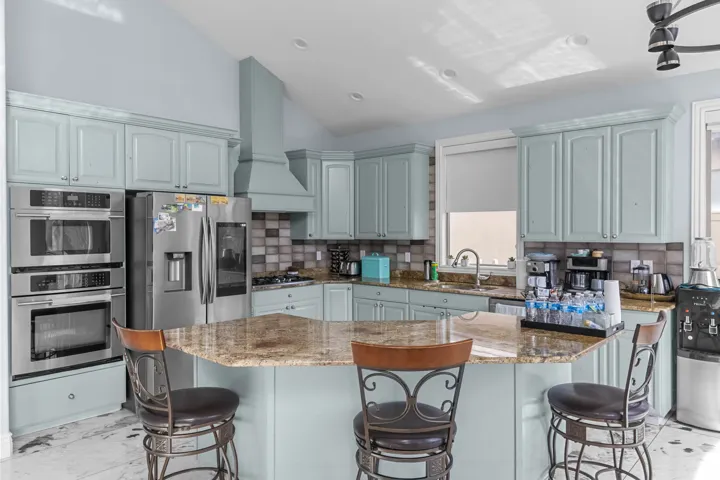 Kitchen with vaulted ceiling, light stone counters, stainless steel appliances, a breakfast bar area, and decorative backsplash