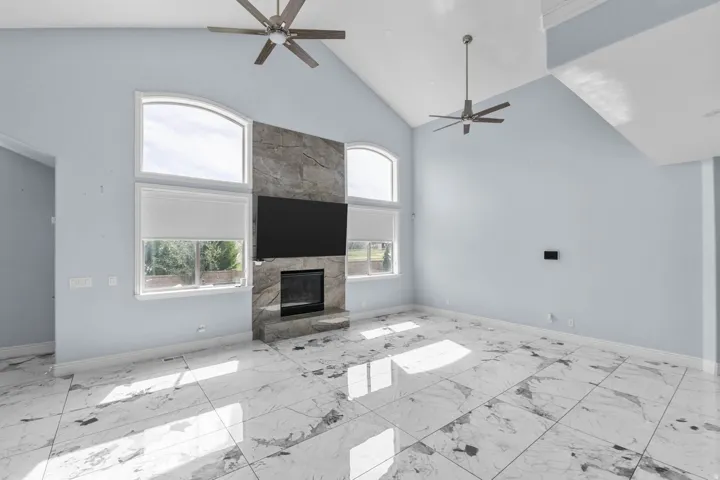 Unfurnished living room featuring a ceiling fan, a large fireplace, and vaulted ceiling