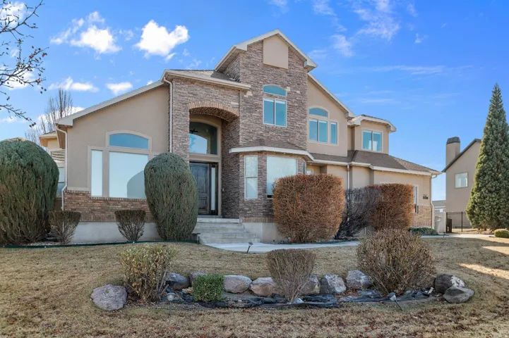View of front facade featuring stucco siding, a front yard, and stone siding
