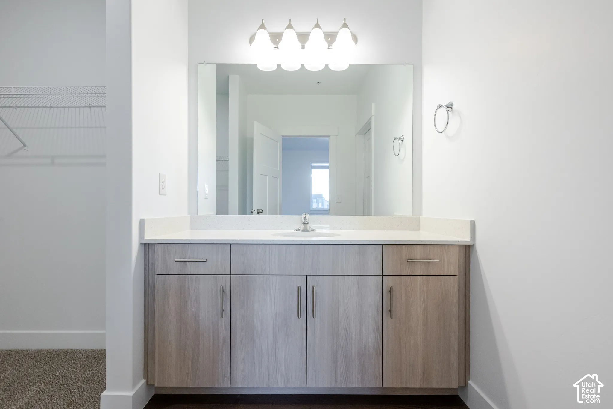 Vanity featuring light wood-finish cabinetry, solid surface countertop, integrated sink, large wall-mounted mirror, and four-bulb light fixture