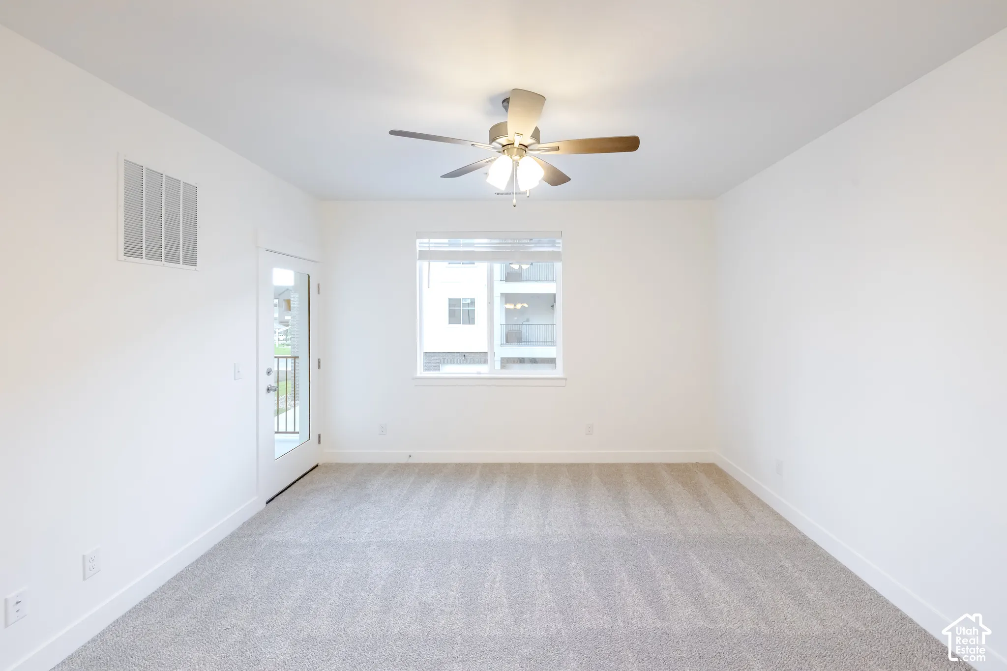 Neutral wall-to-wall carpeting, ceiling-mounted light fixture with integrated fan, and glass-paneled exterior door