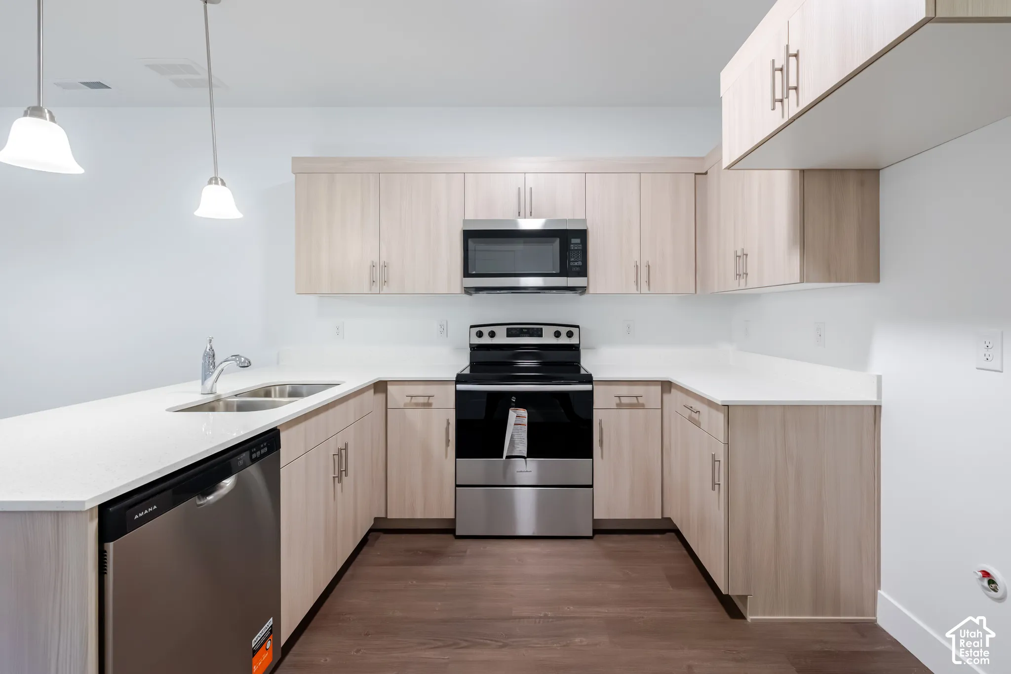Kitchen featuring light-finish cabinetry, white countertops, stainless steel appliances, wood-finish flooring, and dual hanging pendant lights