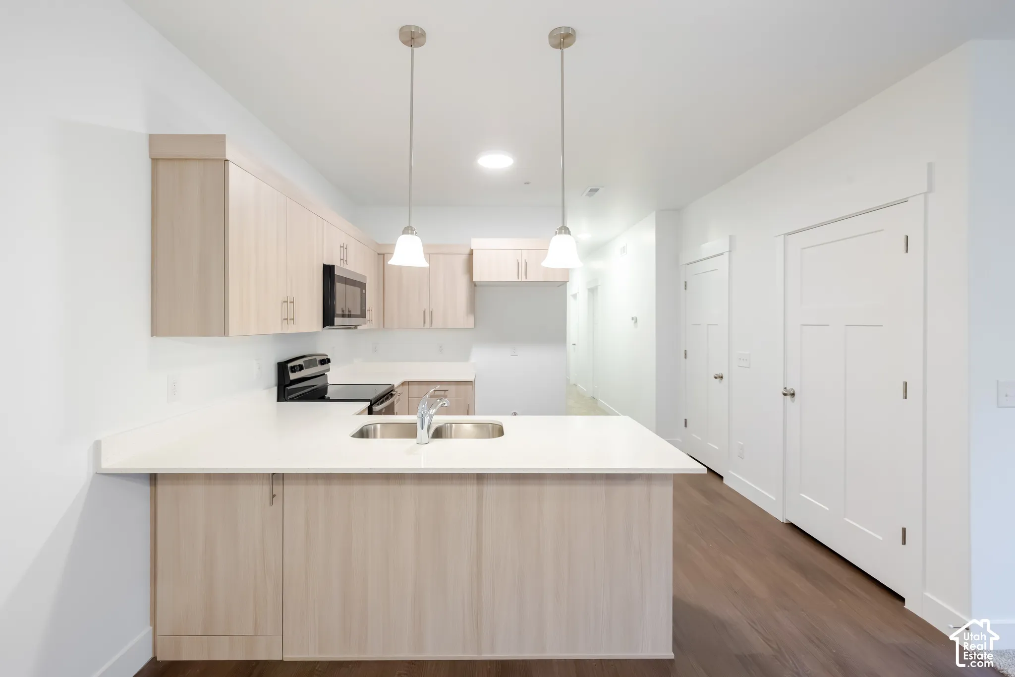 Kitchen featuring light-toned cabinetry, quartz countertops, a double-basin undermount sink, dual pendant lighting, and wood-finish flooring
