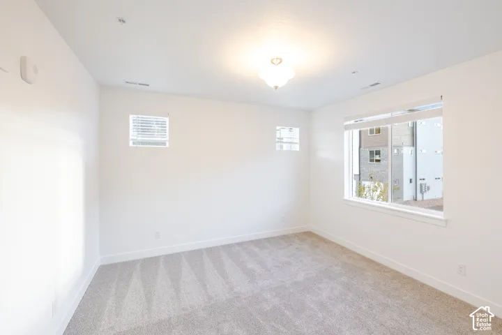Neutral-toned carpeting, high-reaching ceilings, large window with horizontal blinds, dual high-set windows, and a central ceiling-mounted light fixture