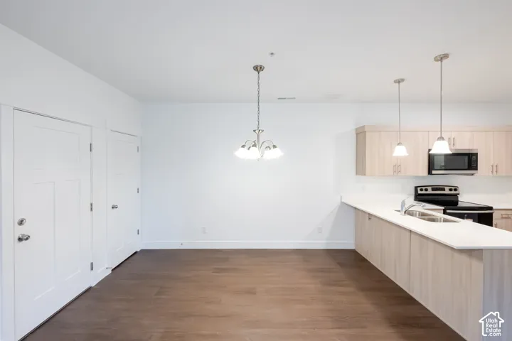 Open-concept kitchen featuring light-toned cabinetry, light-colored countertops, wood-finish flooring, two hanging pendant lights, and a multi-bulb chandelier