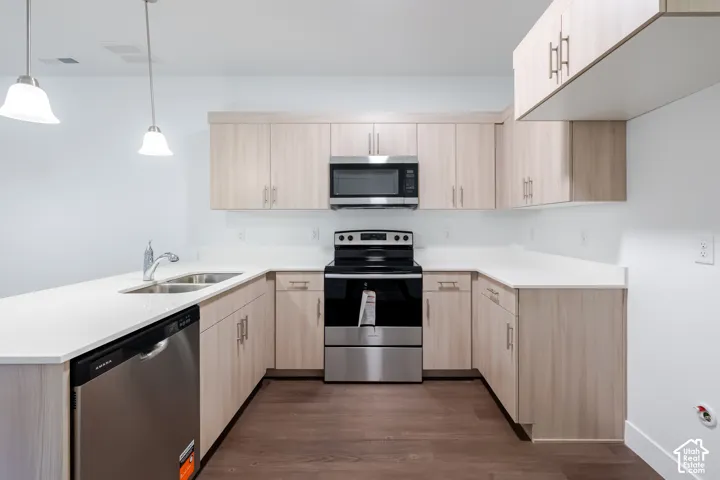 Kitchen featuring light-finish cabinetry, white countertops, stainless steel appliances, wood-finish flooring, and dual hanging pendant lights