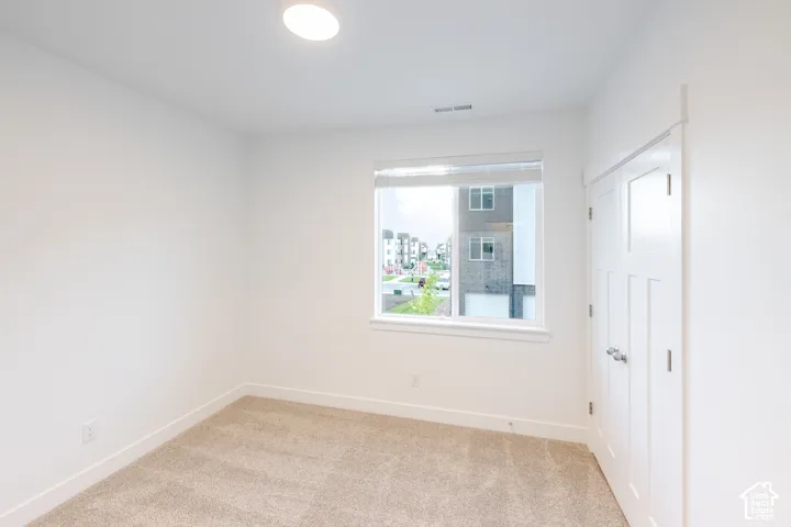 Neutral-toned wall-to-wall carpeting, single-pane window with white roller shade, and double-door closet with satin-nickel hardware