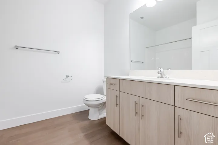 Bathroom featuring wood-finish cabinetry, light-toned countertop with an integrated basin, large frameless mirror, chrome hardware, and wood-finish flooring