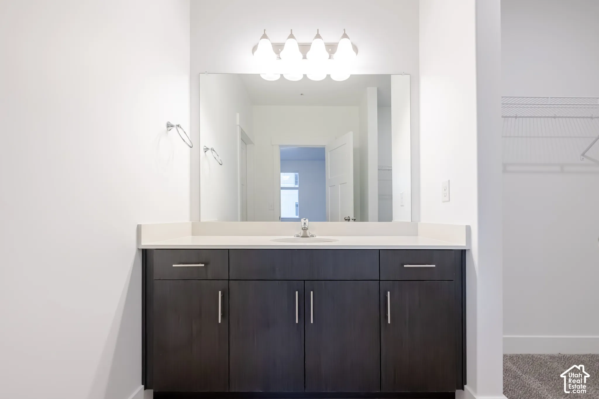 Dark wood-finish cabinetry featuring brushed nickel hardware, expansive countertop with an integrated basin, large wall-mounted mirror, and multi-bulb polished chrome vanity lighting