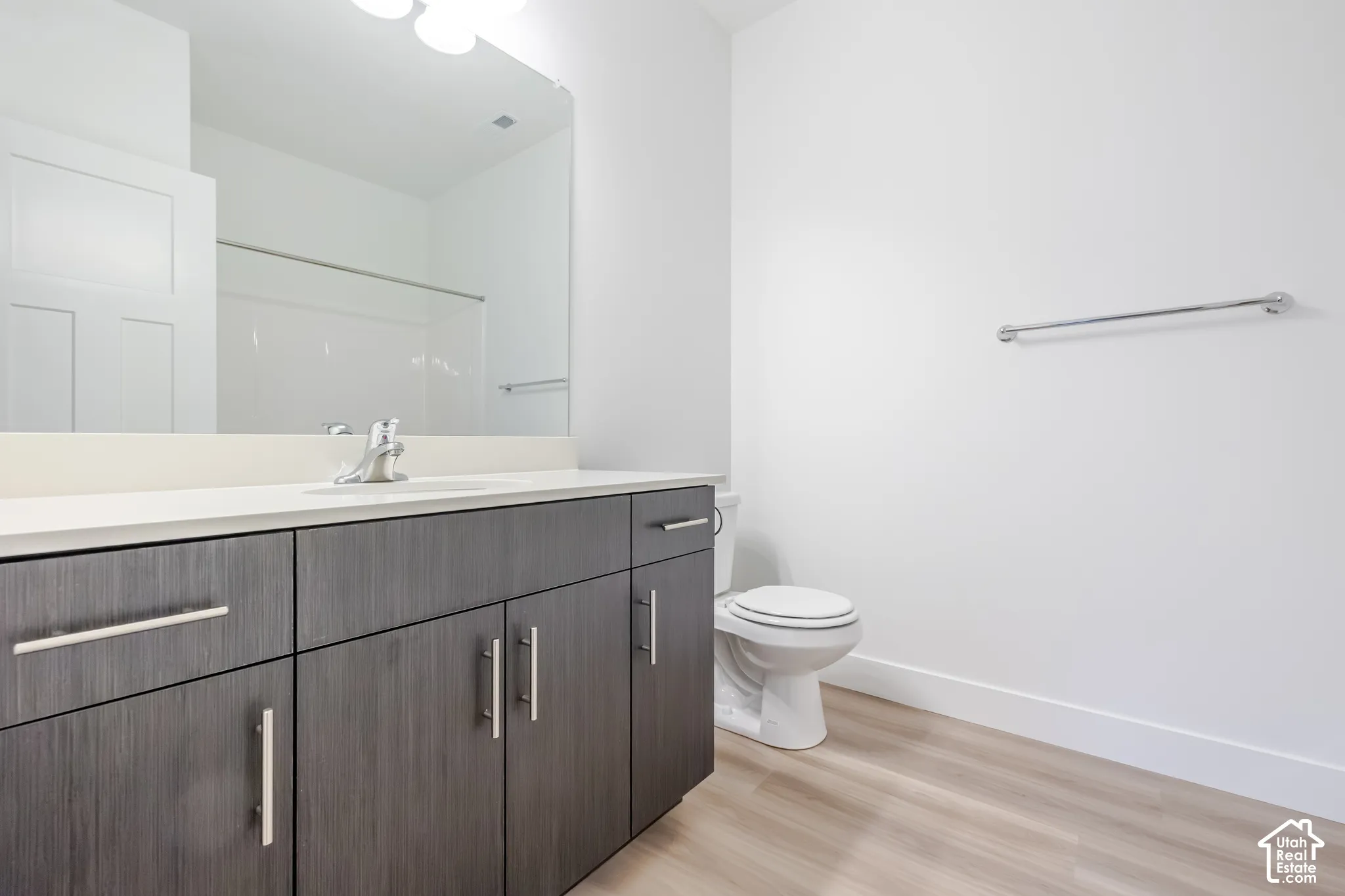 Dark-toned vanity with integrated stone-finish countertop, undermount sink, brushed nickel hardware, expansive vanity mirror, and wood-finish flooring