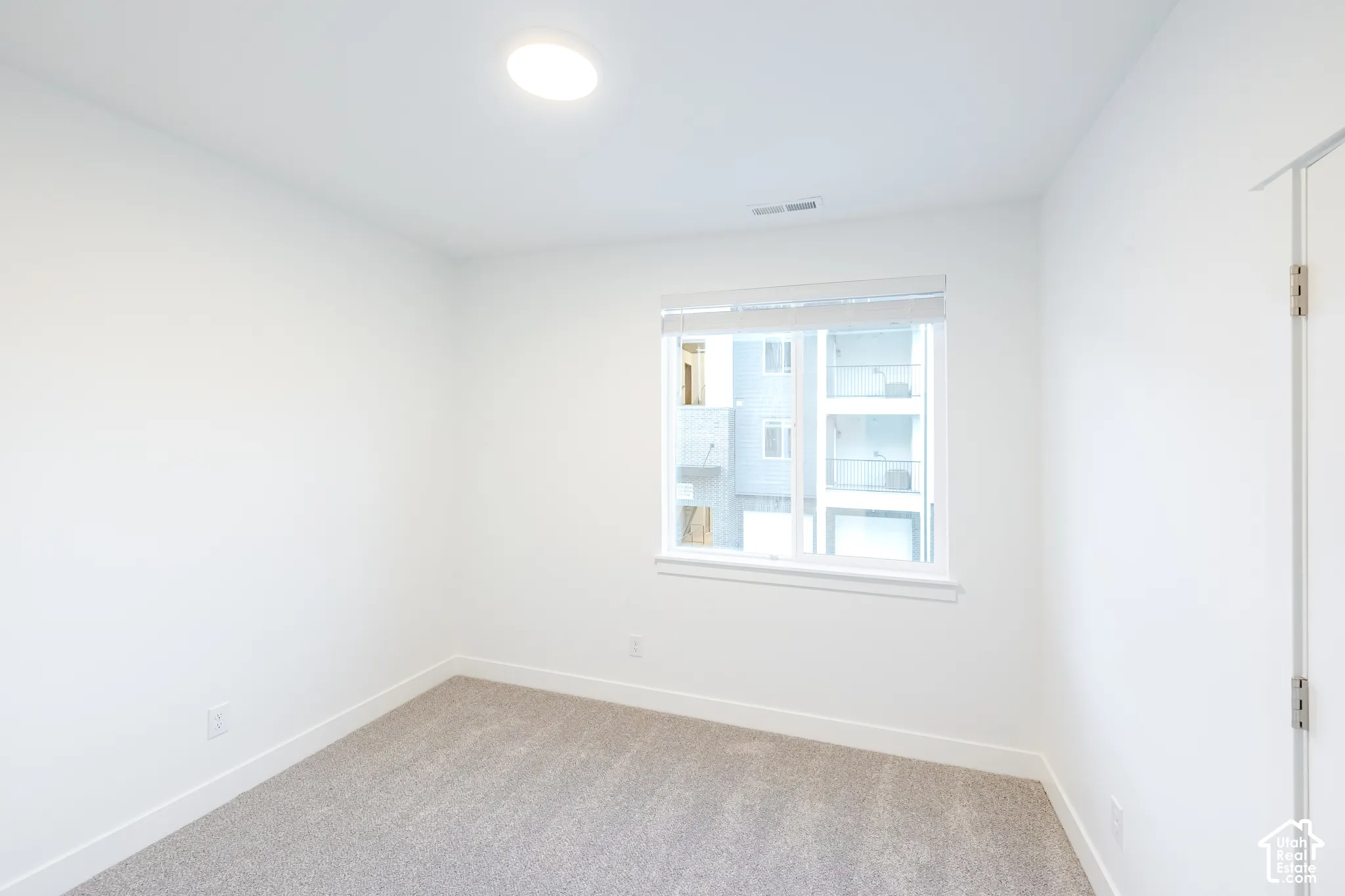 Neutral-toned carpeting, crisp white wall finishes, energy-efficient flush-mount lighting, and a single-pane window with custom blinds