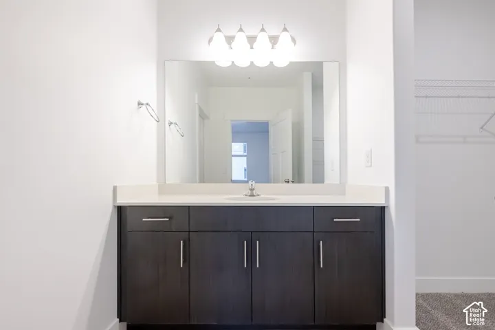 Dark wood-finish cabinetry featuring brushed nickel hardware, expansive countertop with an integrated basin, large wall-mounted mirror, and multi-bulb polished chrome vanity lighting