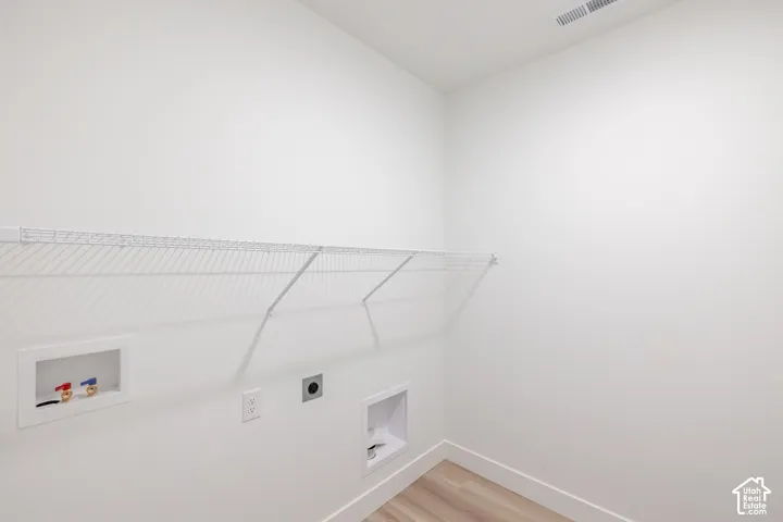 Laundry space featuring wood-finish flooring, white walls, and built-in wire shelving