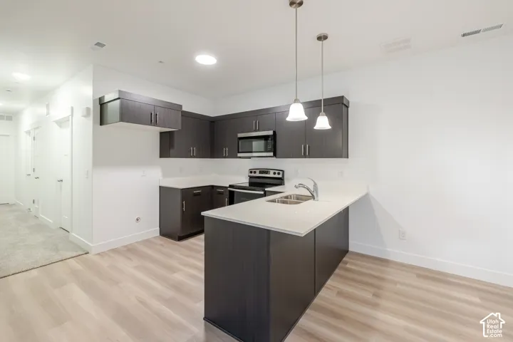 Kitchen featuring dark cabinetry, solid-surface countertops, wood-finish flooring, dual-basin sink, and pendant lighting