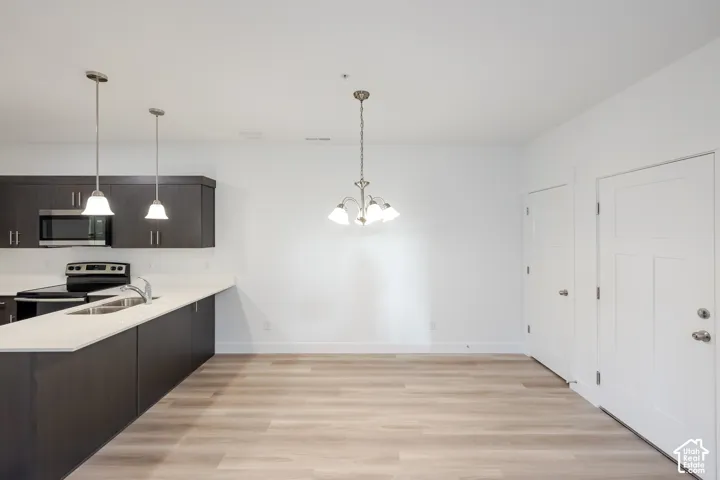 Kitchen featuring dark cabinetry, solid-surface countertops, wood-finish flooring, and dual hanging pendant lights