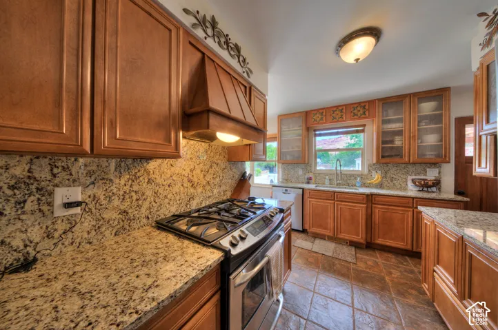 Kitchen featuring Gas stove/oven with hood, stone tile floors, Granite countertops, and glass fronted cabinets