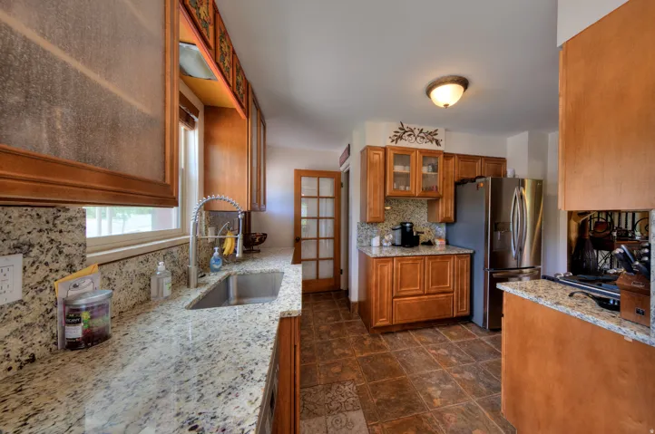 Kitchen featuring glass fronted cabinets, wood finish cabinets, stainless steel refrigerator, and Granite countertops