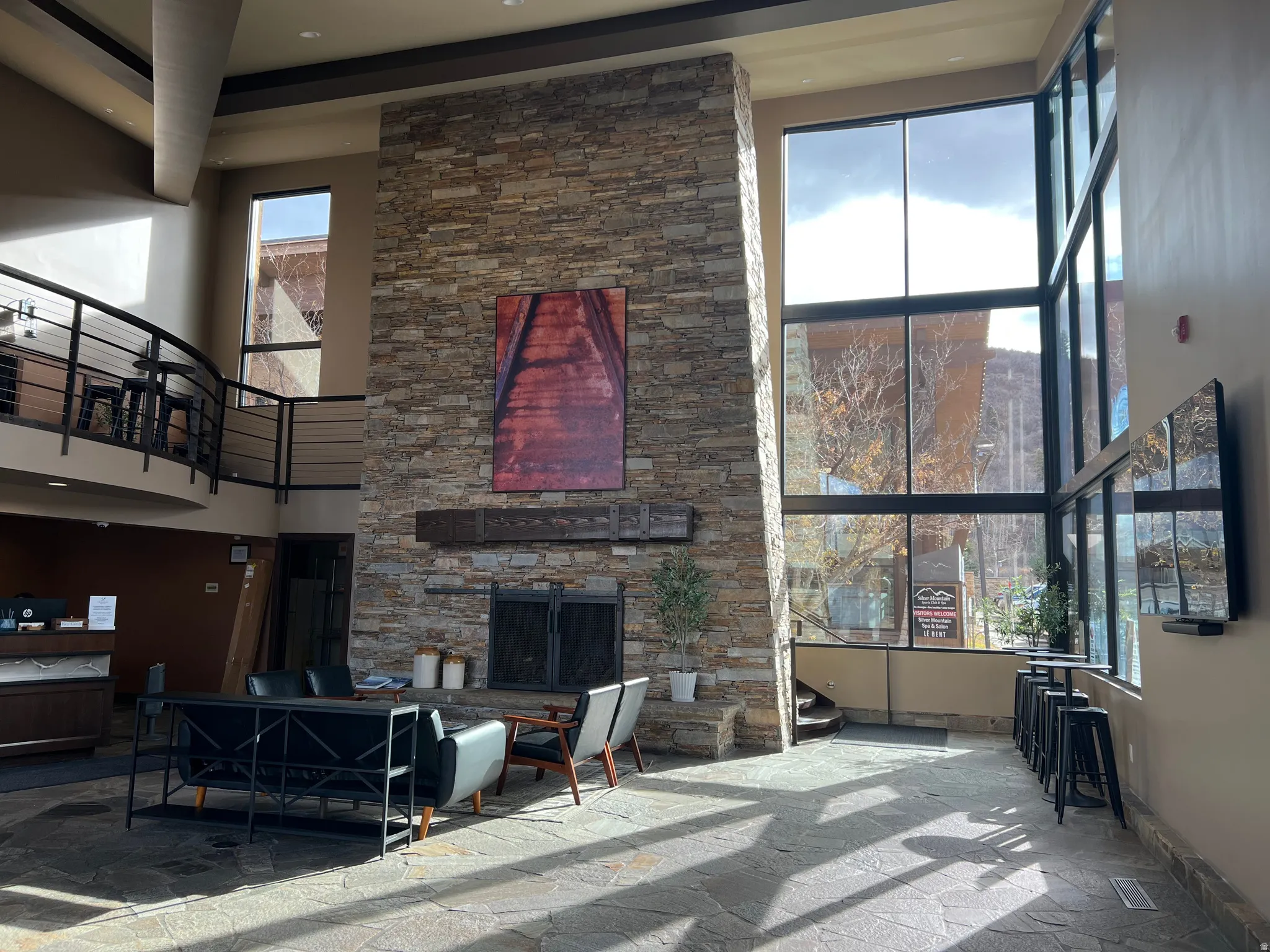Living room featuring a high ceiling, stone finish flooring, an outdoor stone fireplace, and recessed lighting