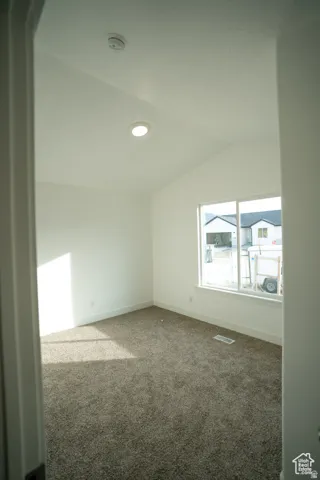 Carpeted empty room with vaulted ceiling and baseboards