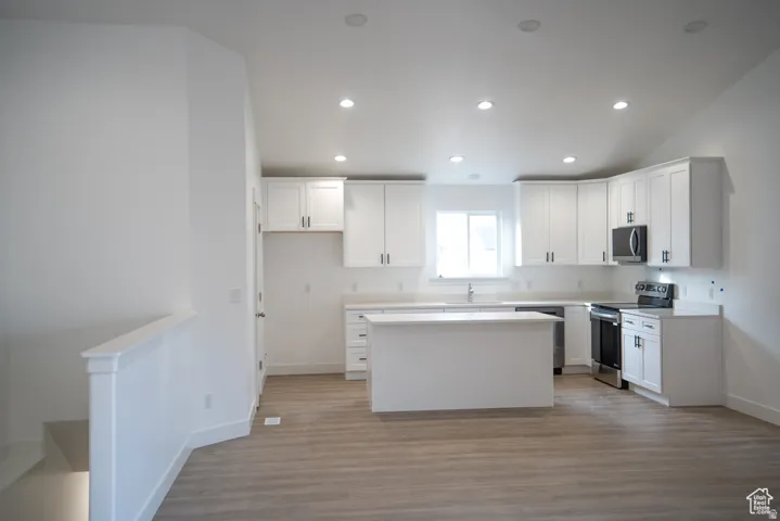 Kitchen featuring stainless steel appliances, white cabinetry, a center island, light countertops, and recessed lighting