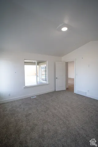 Carpeted empty room with baseboards and lofted ceiling