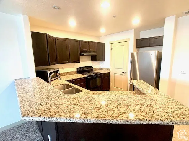 Kitchen with dark wood finish cabinetry, stainless steel appliances, light stone counters, a peninsula, and recessed lighting
