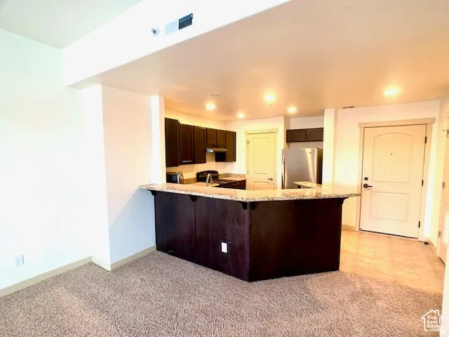 Kitchen featuring a peninsula, a breakfast bar area, dark wood finish cabinets, freestanding refrigerator, and light stone counters