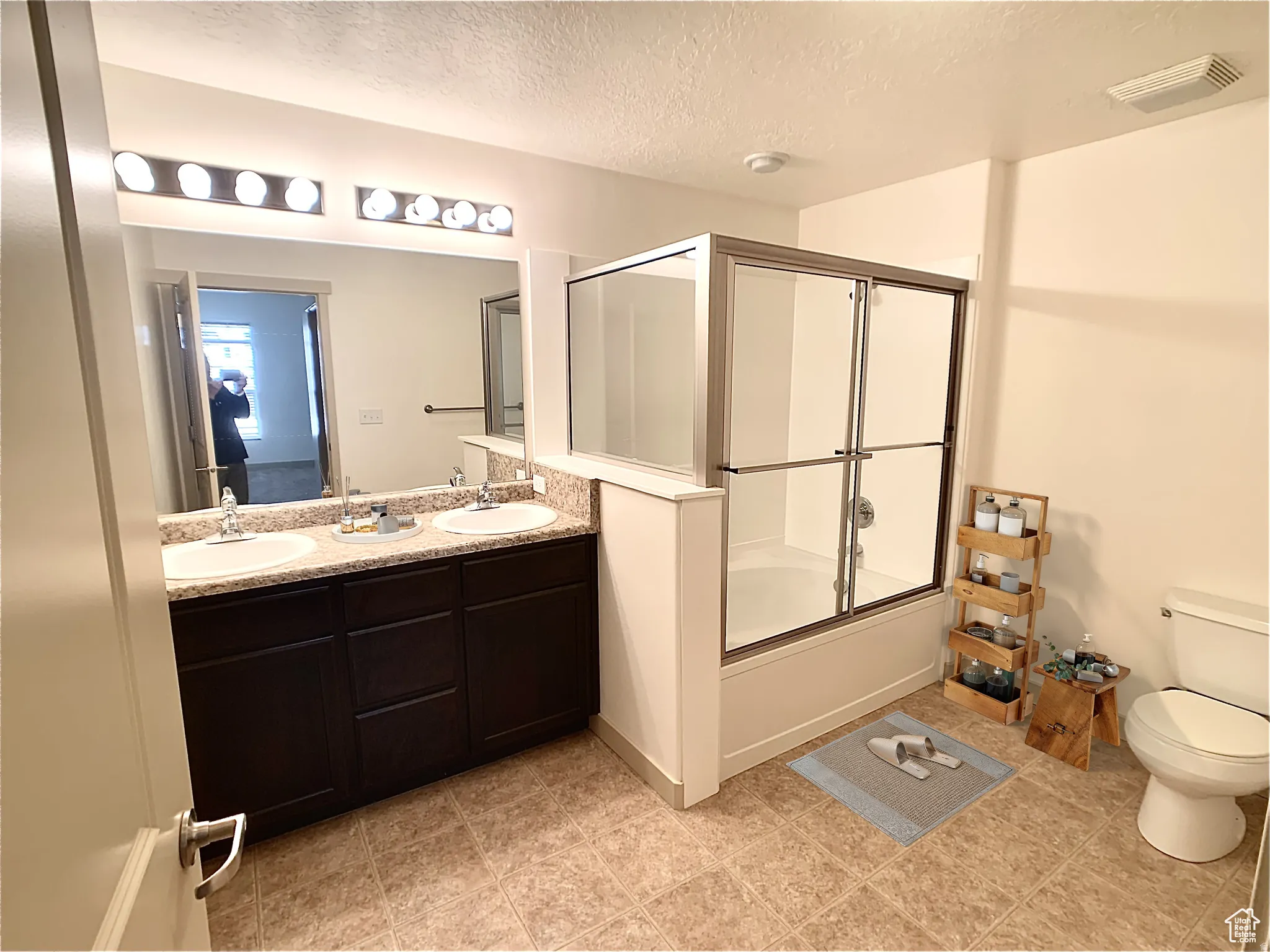 Full bathroom featuring a textured ceiling, enclosed tub / shower combo, and double vanity