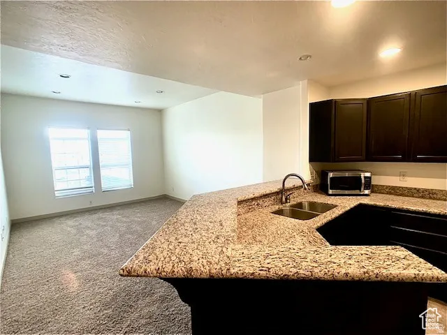Kitchen featuring carpet, a peninsula, light stone counters, open floor plan, and stainless steel microwave