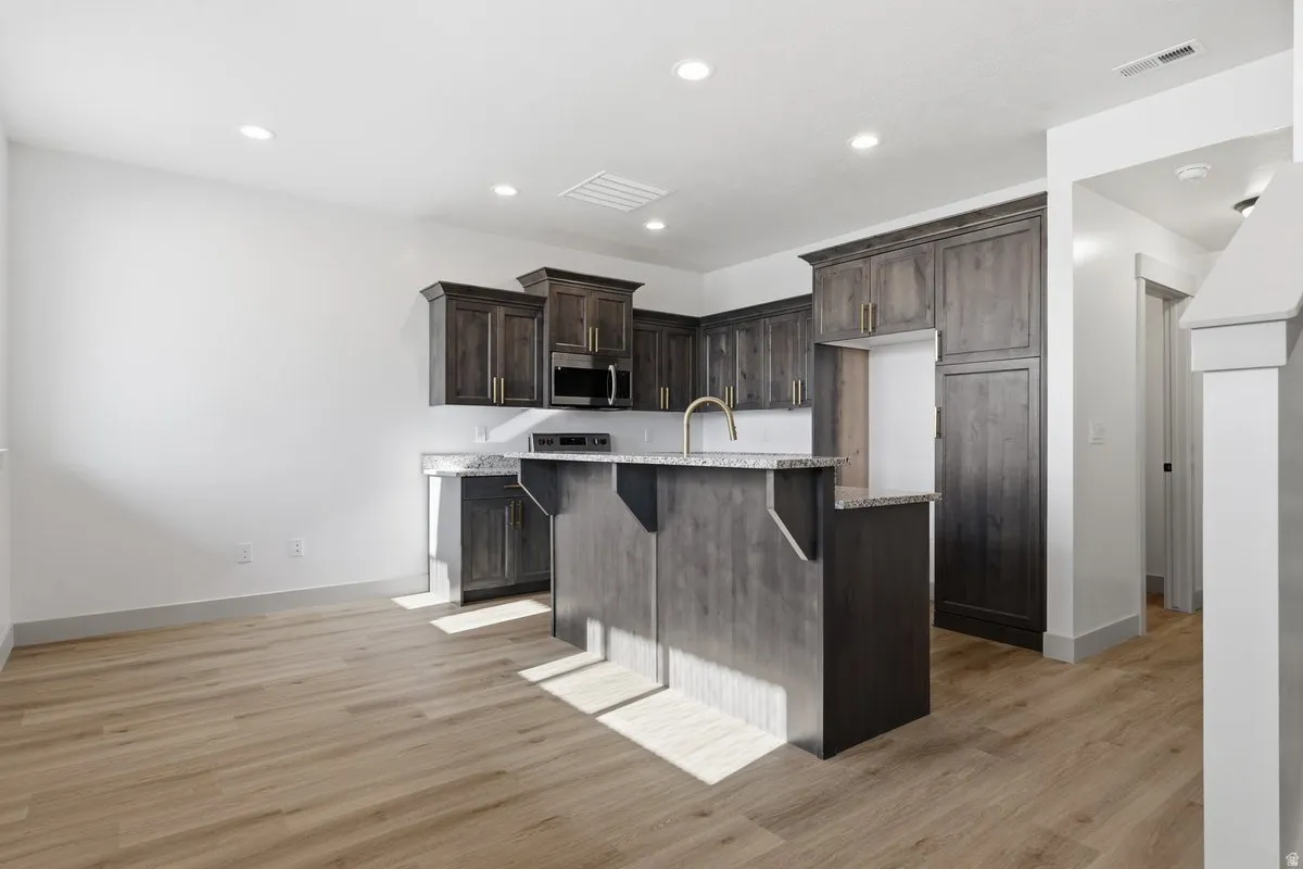 Kitchen featuring a breakfast bar, an island with sink, dark wood finish cabinetry, light wood-style flooring, and recessed lighting