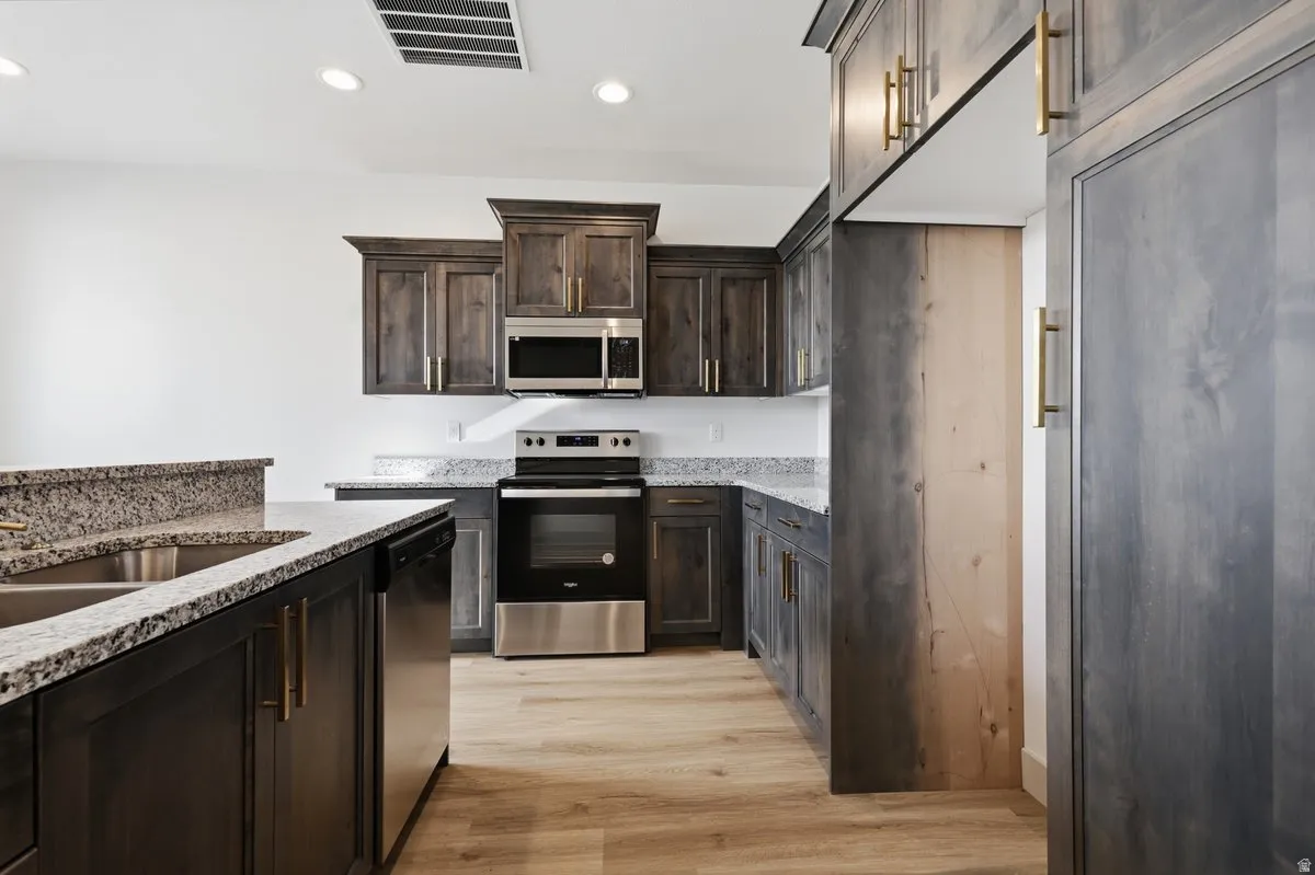 Kitchen featuring stainless steel appliances, dark wood finish cabinetry, light stone counters, light wood-style flooring, and recessed lighting