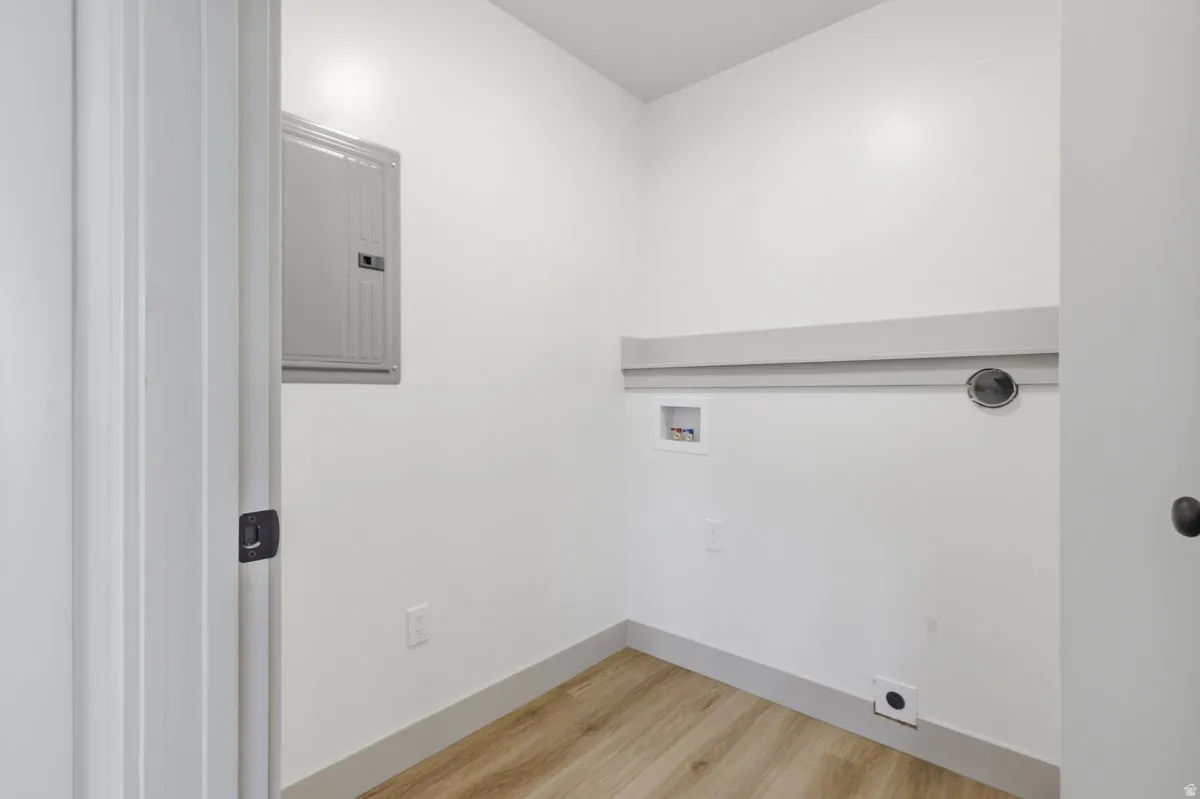 Laundry room with electric panel, light wood-style floors, and hookup for a washing machine