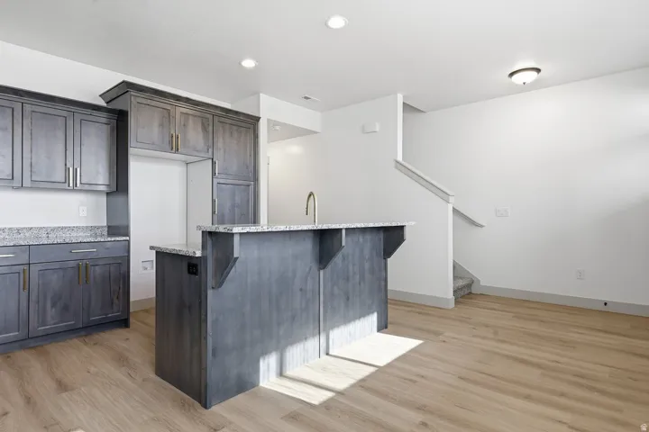 Kitchen with light stone countertops, light wood-style flooring, a kitchen bar, a center island, and dark wood finish cabinets