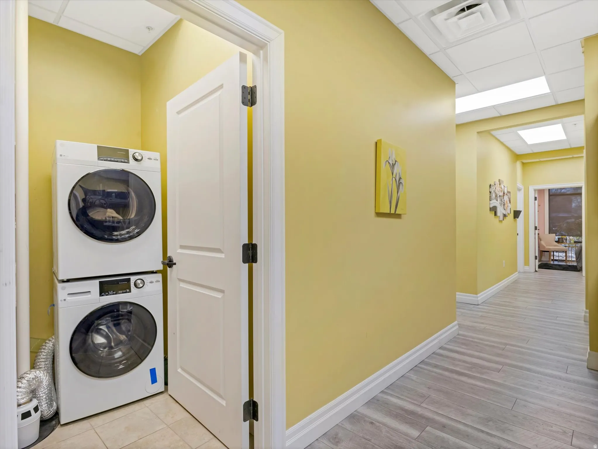 Laundry area with a drop ceiling, stacked washer and dryer, and light wood-type flooring